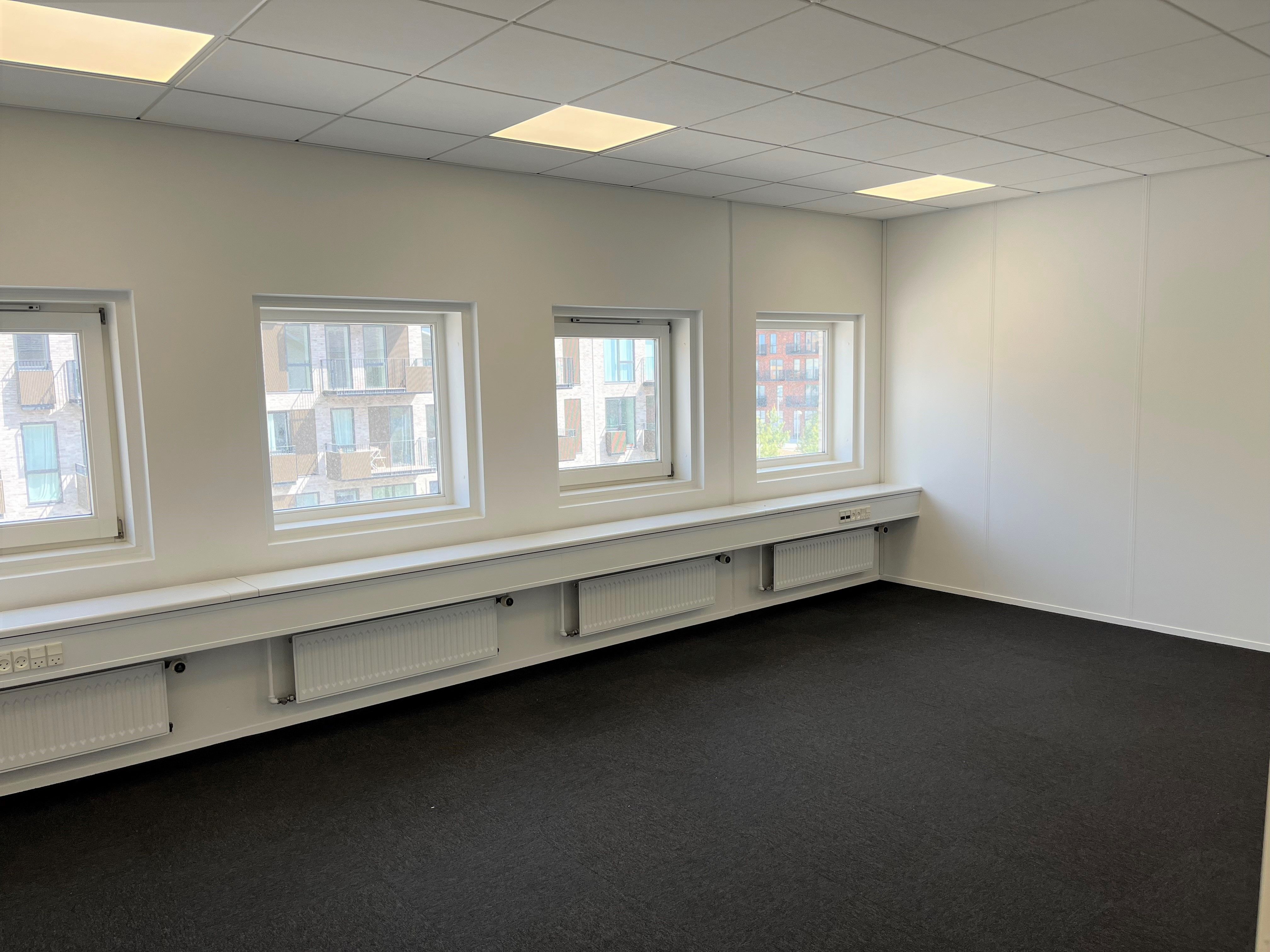 Minimalistisk mødeværelse med hvide vægge og tre vinduer med udsigt til bygninger og grønne træer