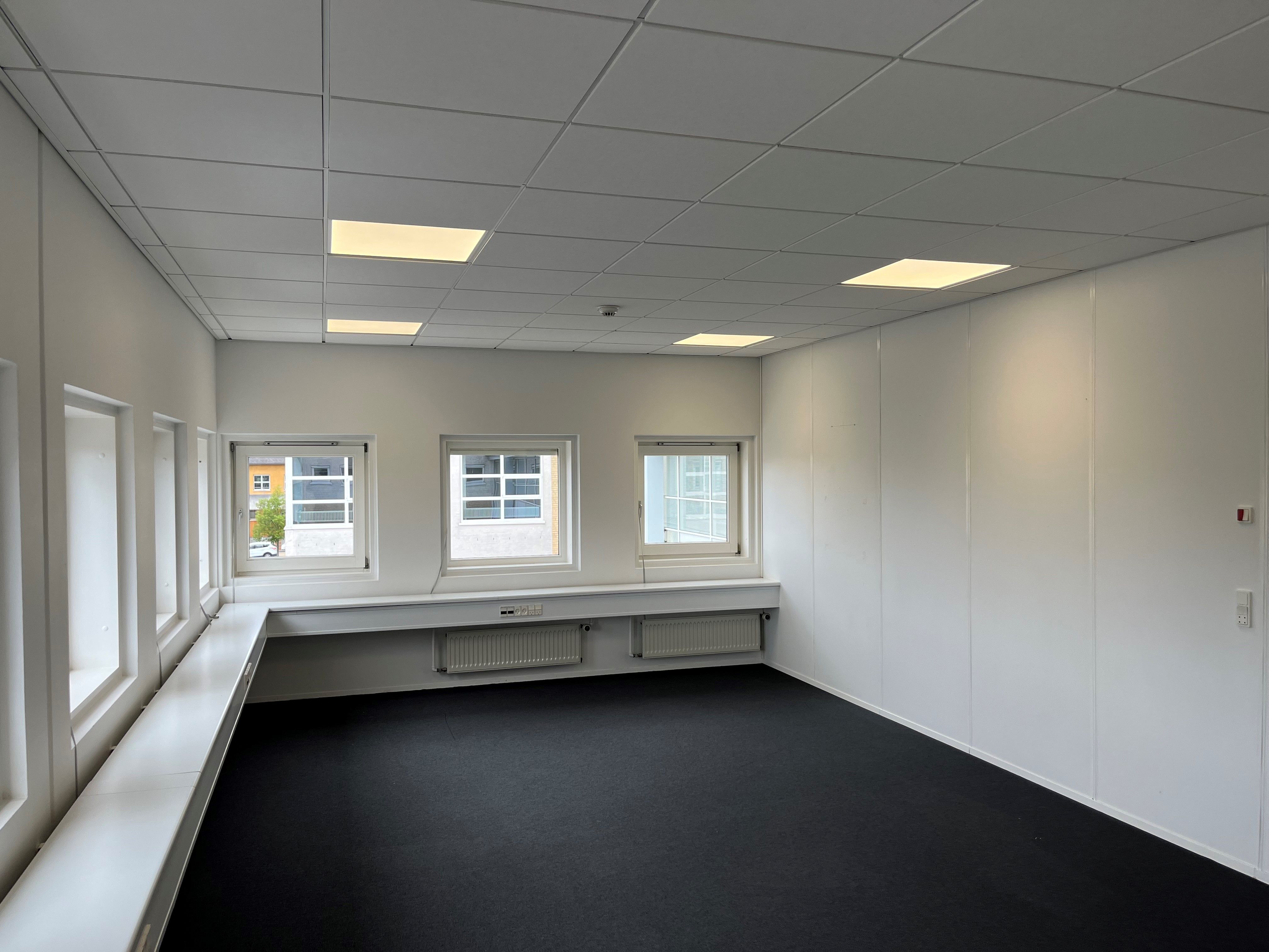 En stor, ren og minimalistisk kontorrum med hvide vægge, hvide loftspaneler og gulvbelægning, der ser smukke og velplejede ud