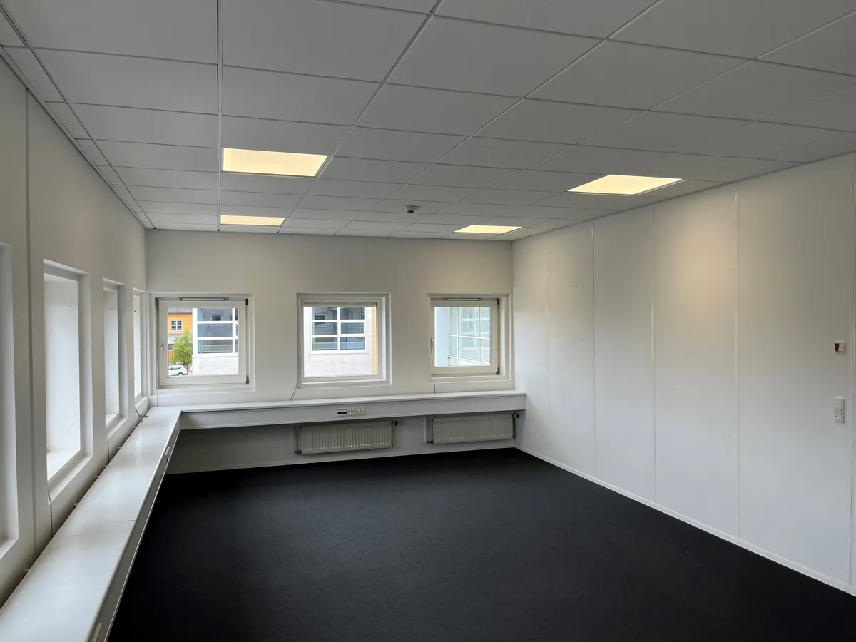 En stor, ren og minimalistisk kontorrum med hvide vægge, hvide loftspaneler og gulvbelægning, der ser smukke og velplejede ud