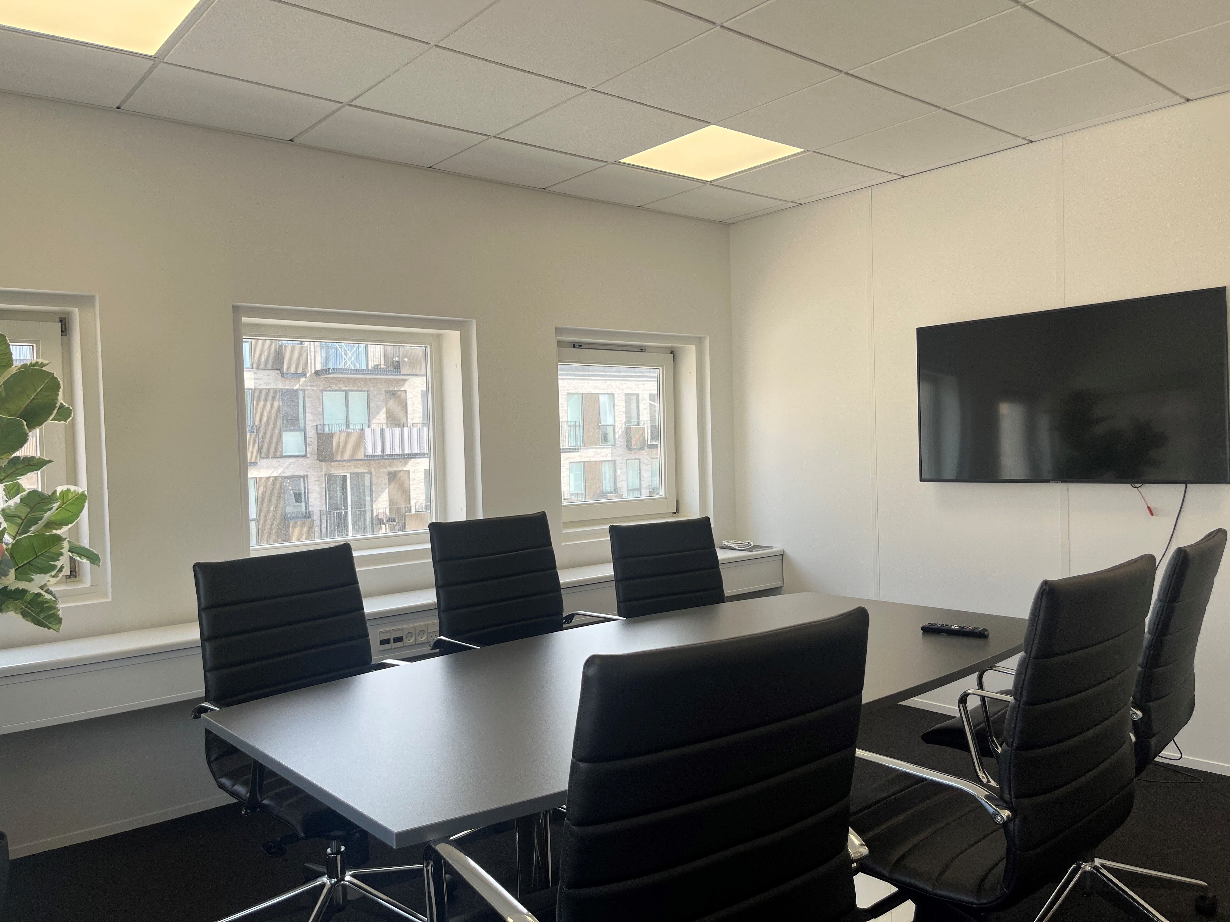 Moderne mødelokale med fem læderstole og en stor fladskærms-tv. Det er et lyse og rummelige kontorfællesskab med store