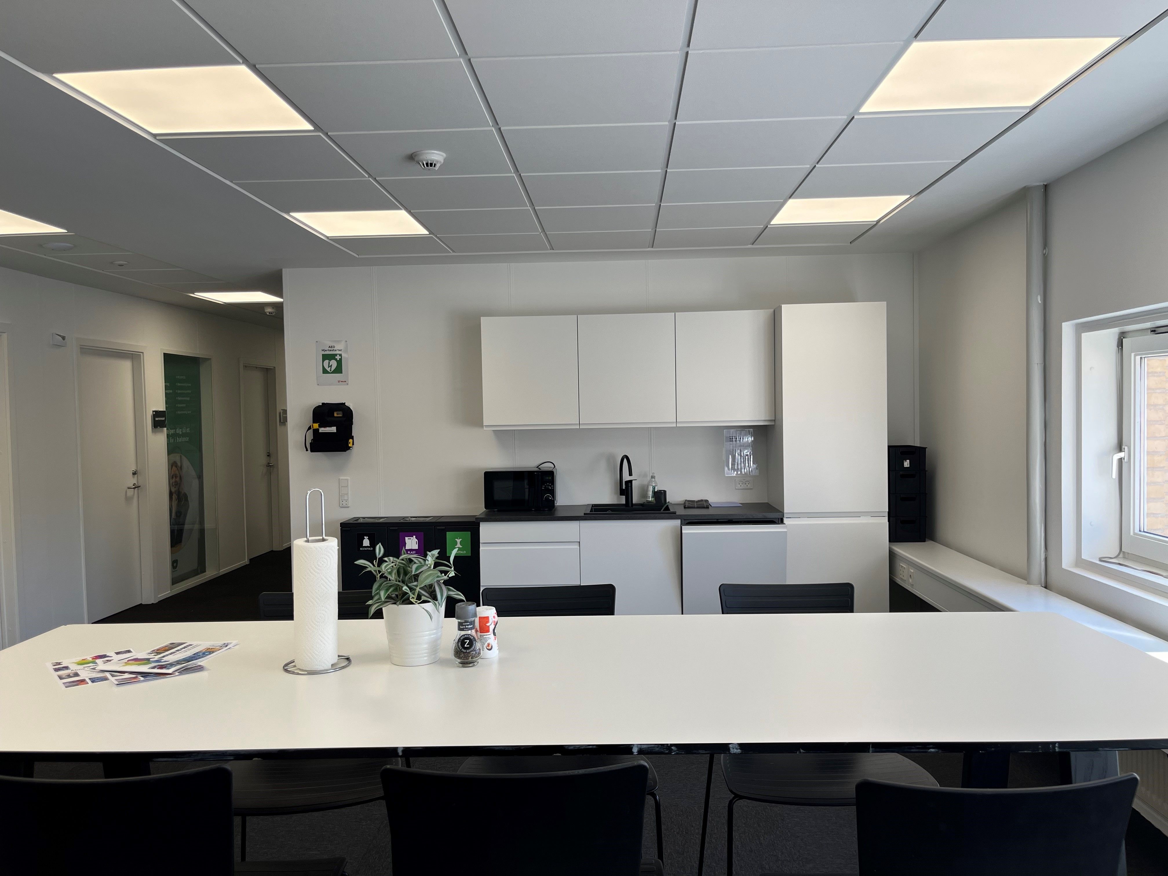 Mødelokale med hvide vægge og loft, fuldt udstyret køkken, og tomme møbler og skrivebord