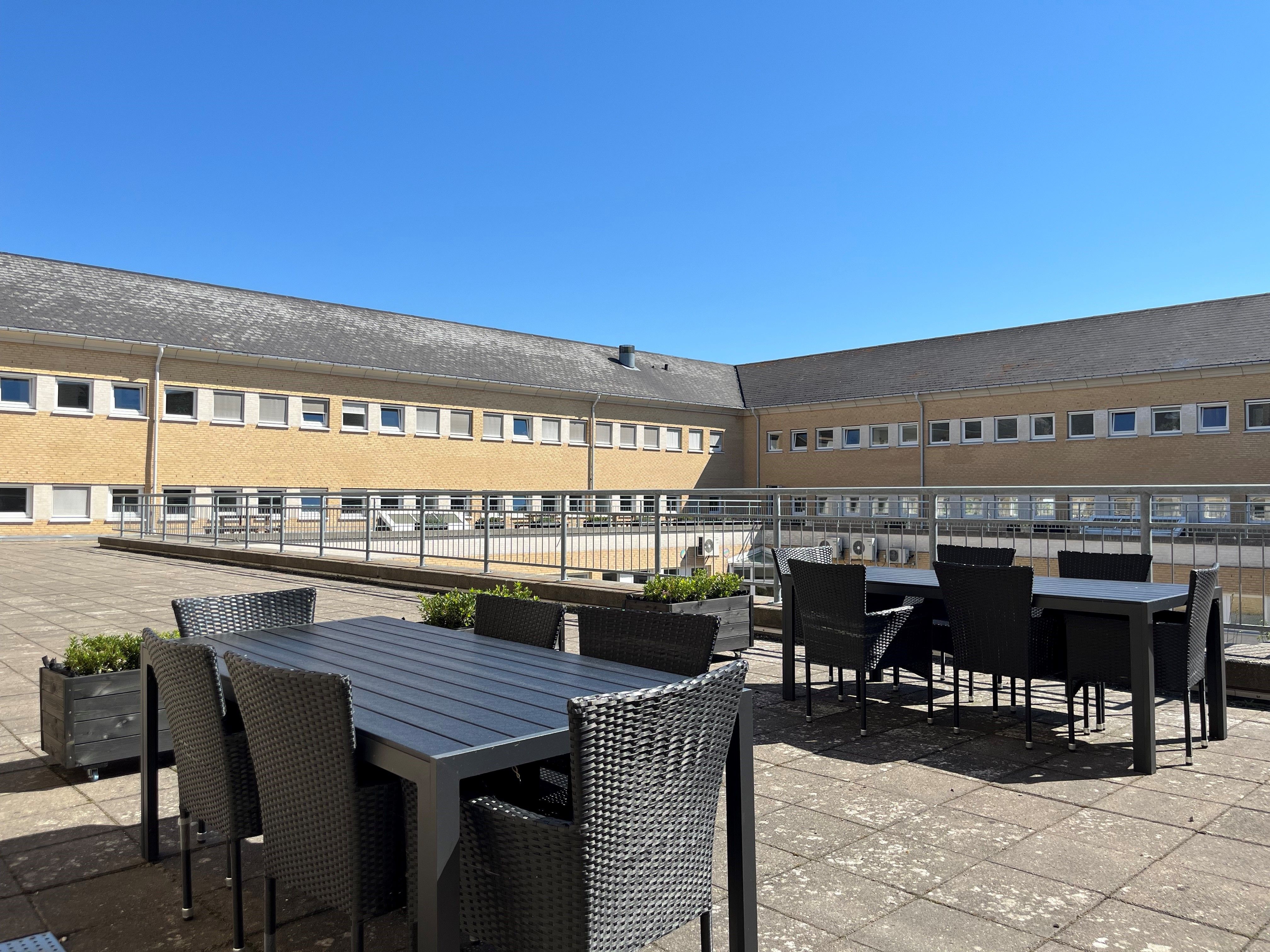 En moderne bygning med terrassehaven og spisestedet med stole og borde under en blå himmel