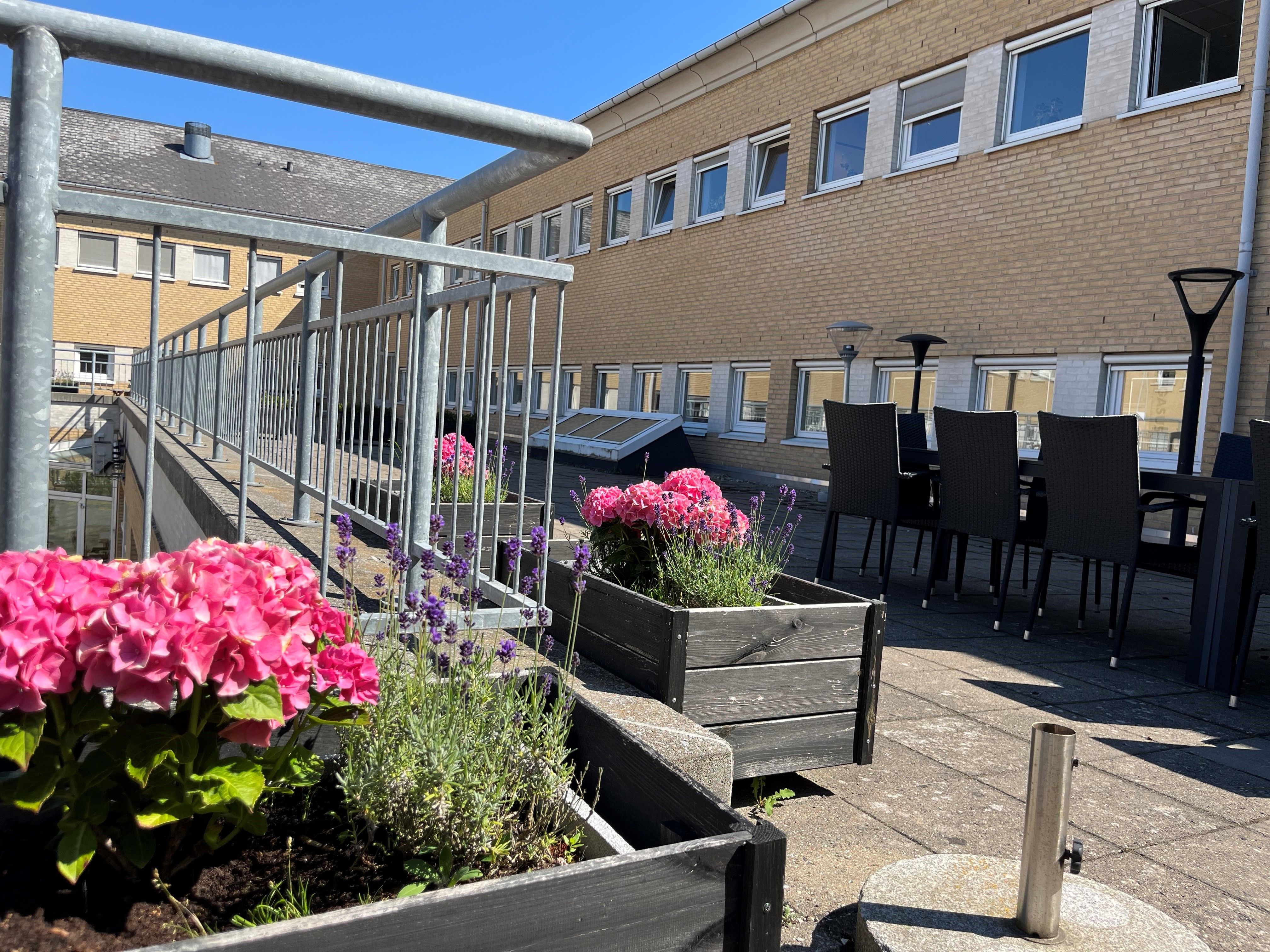 Et værelse med to bænke med blomster og lysekroner på en terrasse med en spiseplads og stole og en gulvbelægning i sten