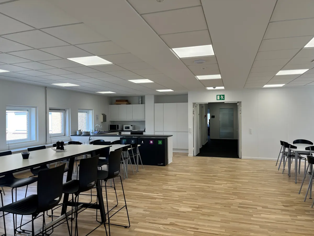 Moderne kontor med højloft og høj kvalitet. Rundt bord med stole og køkken med mikroovn og vask. Adgangsdør til et andet rum.