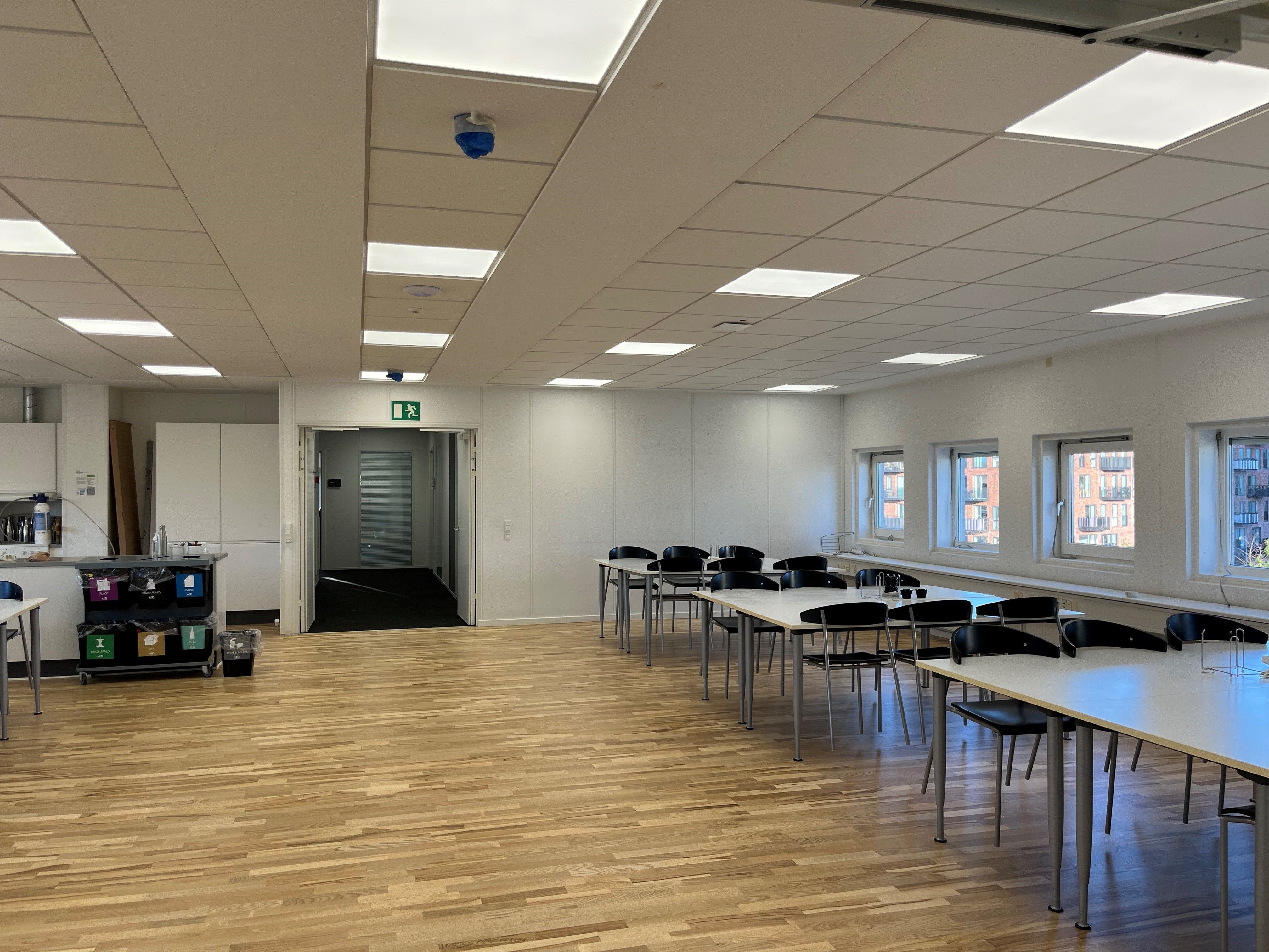 Et moderne kontor med masser af lyse loftspaneler, flere runde runde skriveborde og stole samt en udsigt til byen gennem