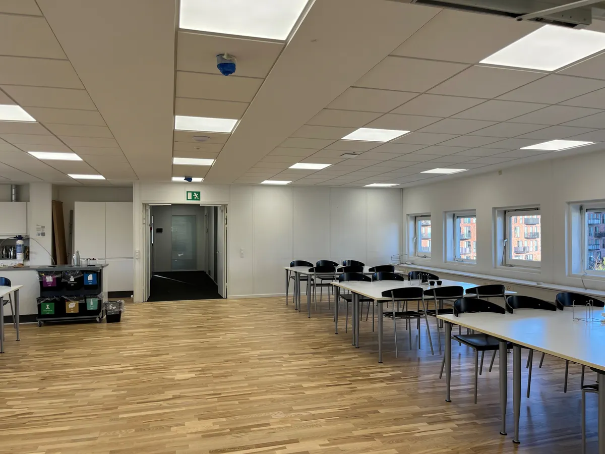 Et moderne kontor med masser af lyse loftspaneler, flere runde runde skriveborde og stole samt en udsigt til byen gennem