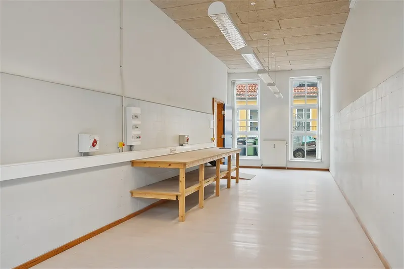 En tom værkstedslokal med lyse gulve, lysegrå vægge og tre lysekroner hængende fra loftet