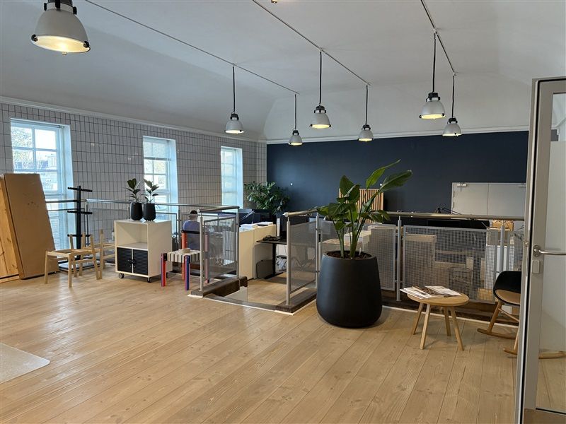 Kontor med højt loft, loftslamper og trægulv med plantepotter og stole i minimalistisk design