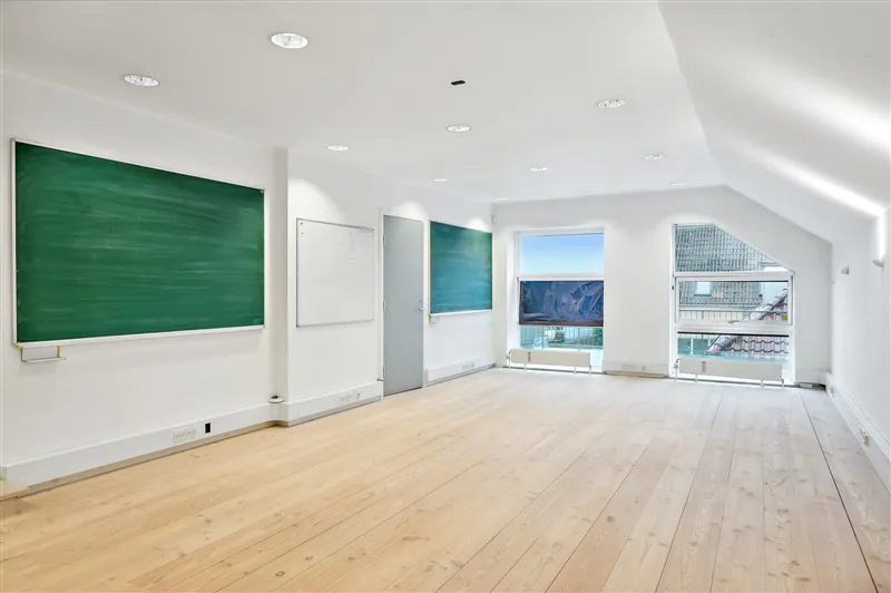 Lys, tomt værelse med lysegul gulv og hvide vægge samt tre skrivebræt og et vindue med udsigt til en balkon