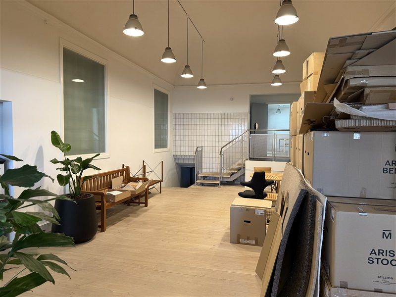 Store bokse står på gulvet i et kontorlokal og man ser en stol og en plante i loftet