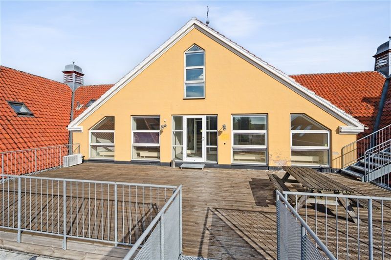 Gult hus med rød tagbelægning og vinduer med terrasse og picnicbord i skoven