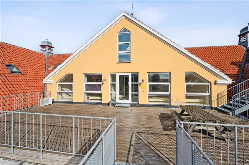 Gult hus med rød tagbelægning og vinduer med terrasse og picnicbord i skoven