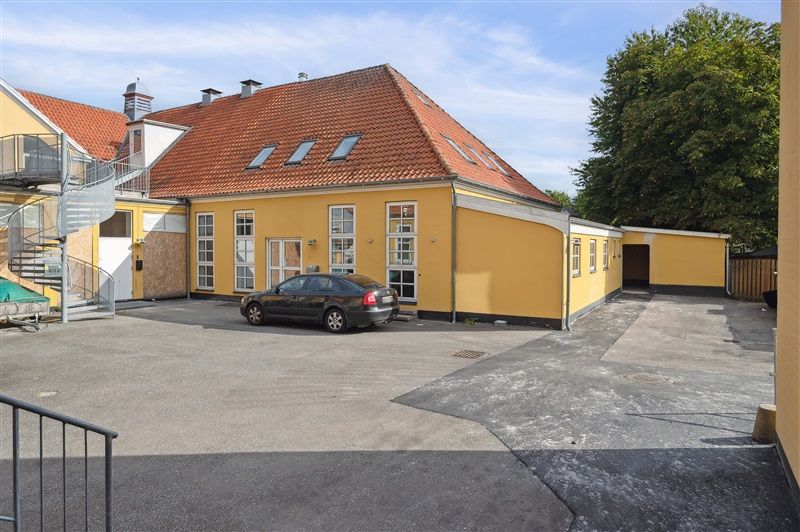 Kontorbyggeri med parkeringsplads foran og spiraltrappe mod loftsrum. Gule vægge og rød tagbeklædning med vinduer og lukket