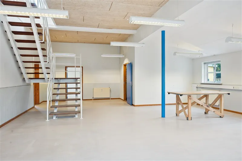 Kontorlokation med lyse vægge og højloft, hvor der er et bord og en trappe til øverste etage