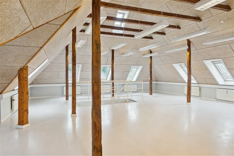 Et rum med lyse loftsbjælke og hvidt loft samt lyse loftsvinduer og hvide vægge