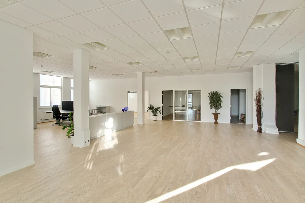 Et ubeboet kontor med hvide vægge, højt til loftet, en reception, flere glasdøre og vinduer samt trægulve