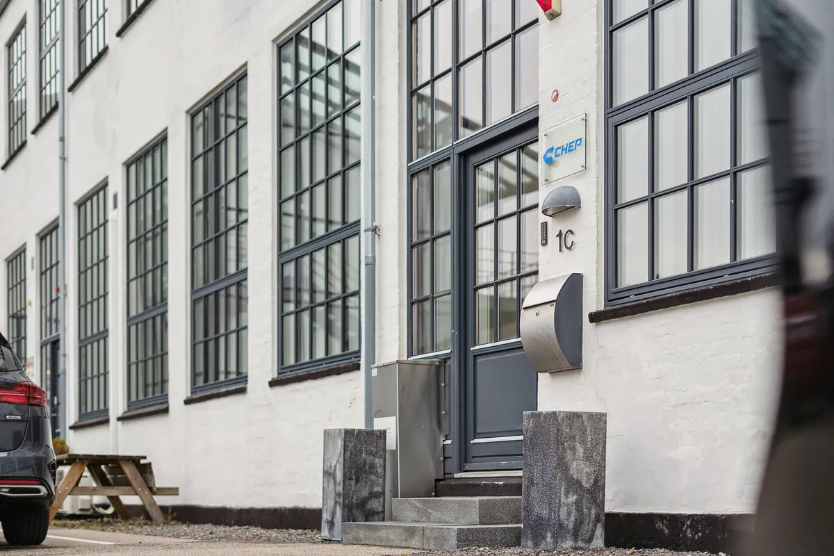 Et moderne kontorblok med glasvinduer og en dør nummer 1C. Der er en stående postkasse og et skilt med CHEP-logoet på væggen.