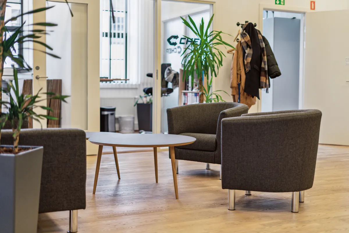 Kontor med tre sæder og en rund bord samt to planter og to jakker hængende på en garderobe