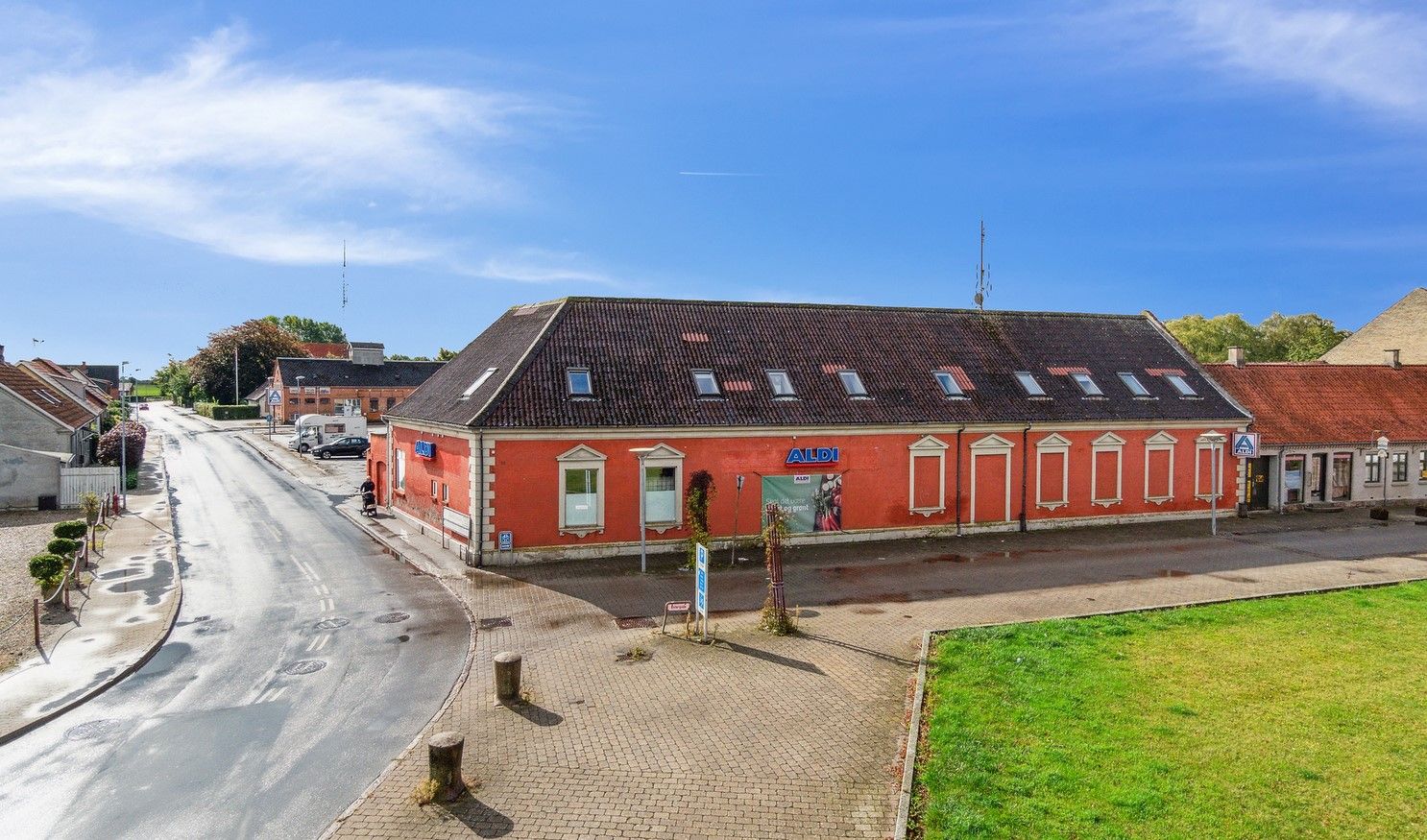 Aldi supermarked med butikker og parkeringspladser samt grønne arealer og busstoppested langs vejen