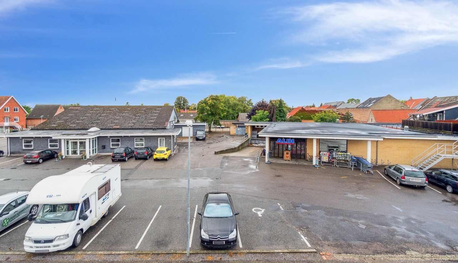Et stort supermarked med faciliteter til parkering og kunder, liggende i et lille dansk byområde med butikker og boliger
