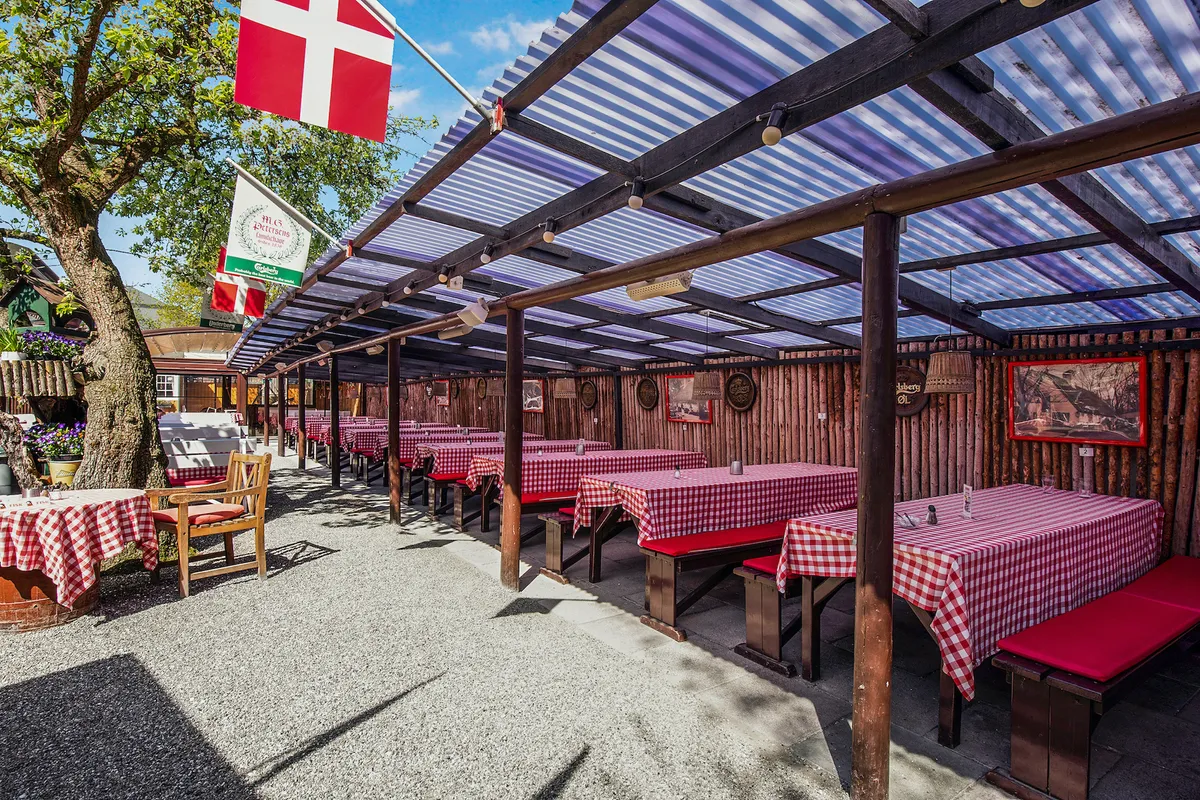 Historisk ølhave med dansk flag, flag og malerier langs væggen, borde og bænke med røde og hvide kuverter, lys i loftet, og