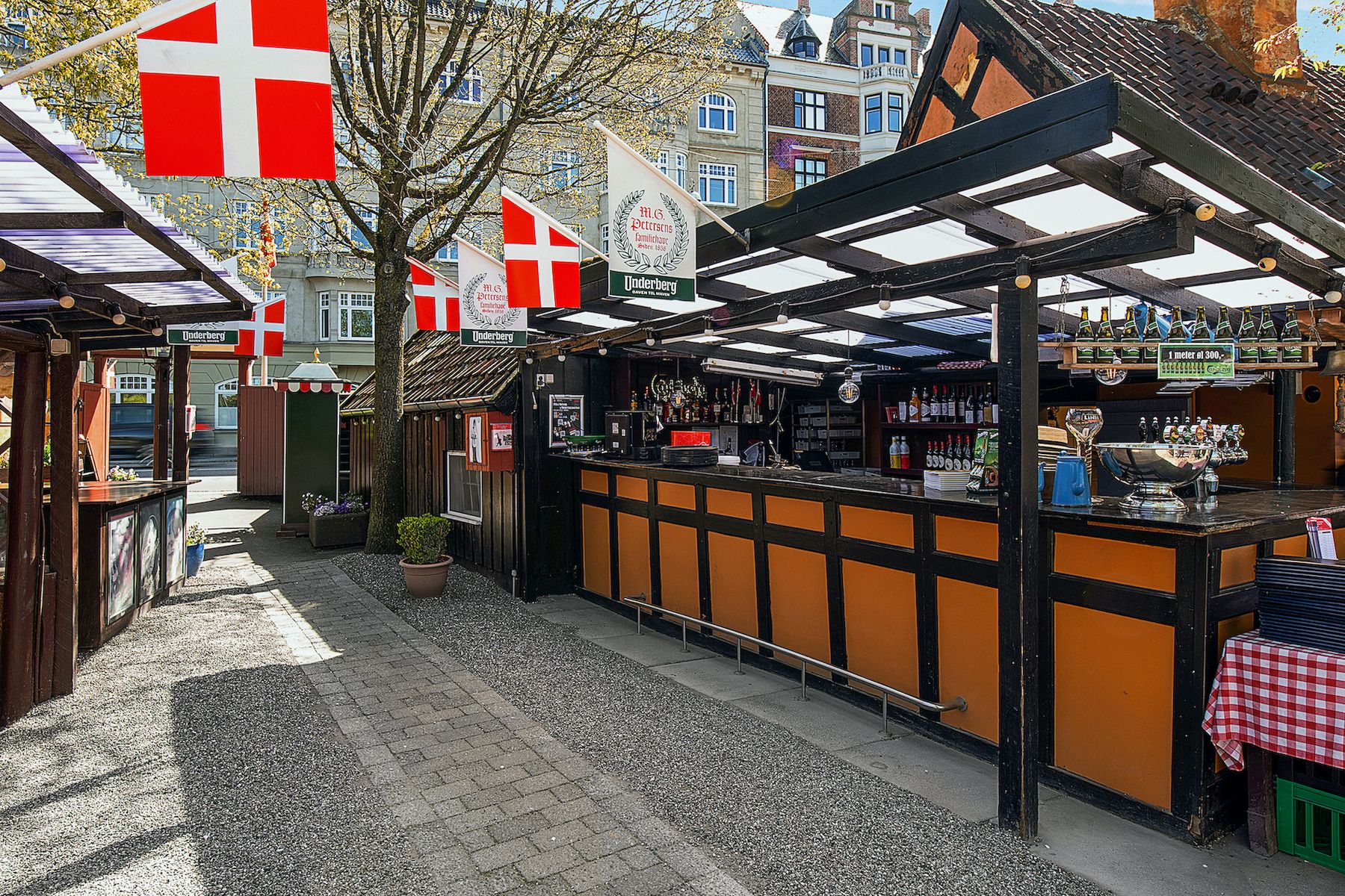 M.G. Petersens Familiehave i Frederiksberg med ølflasker og danske flag, der vender mod en fredelig gade