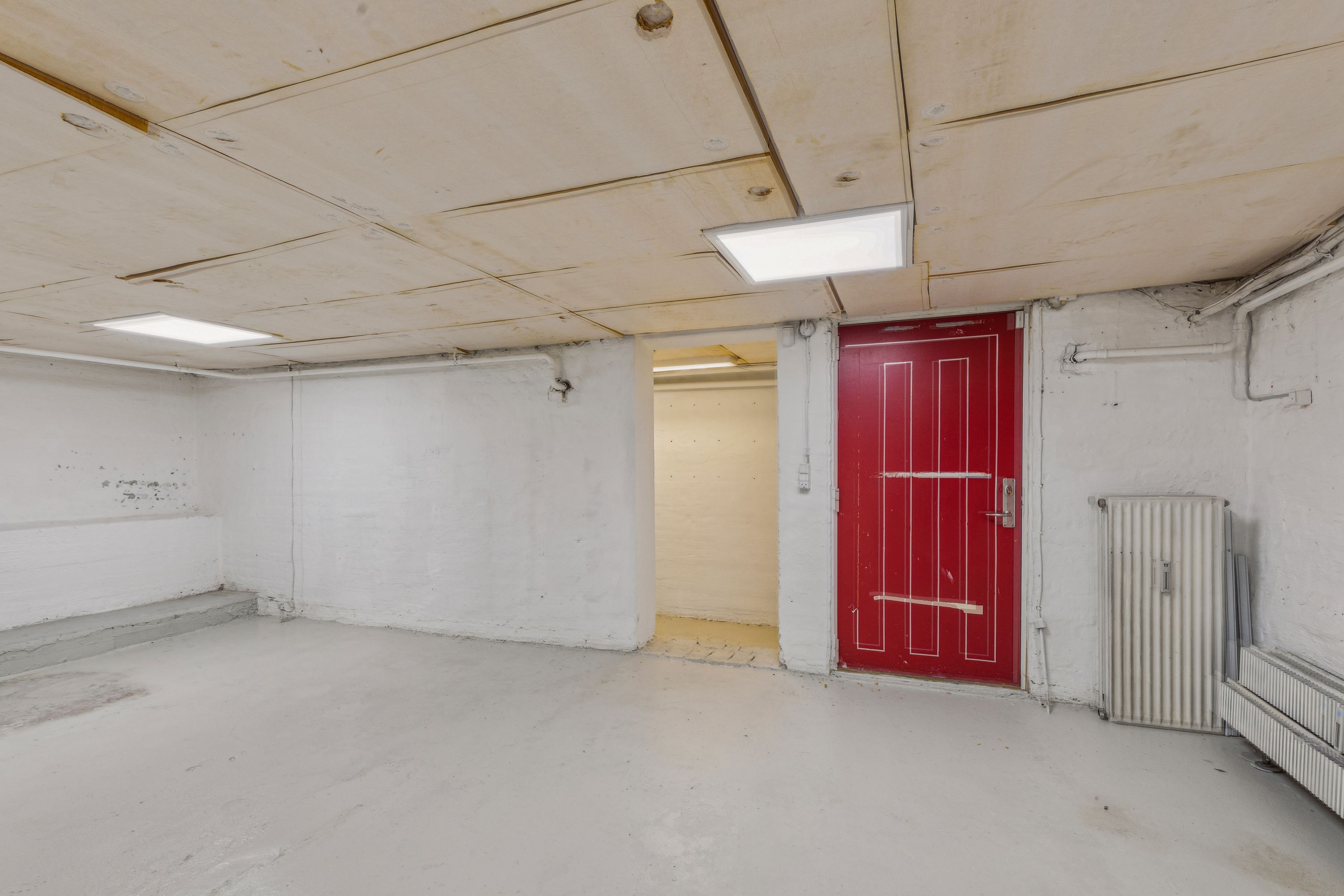 En tom og ren rum med et rød dør og en hvid væg med radiatorer og et lys på loftet