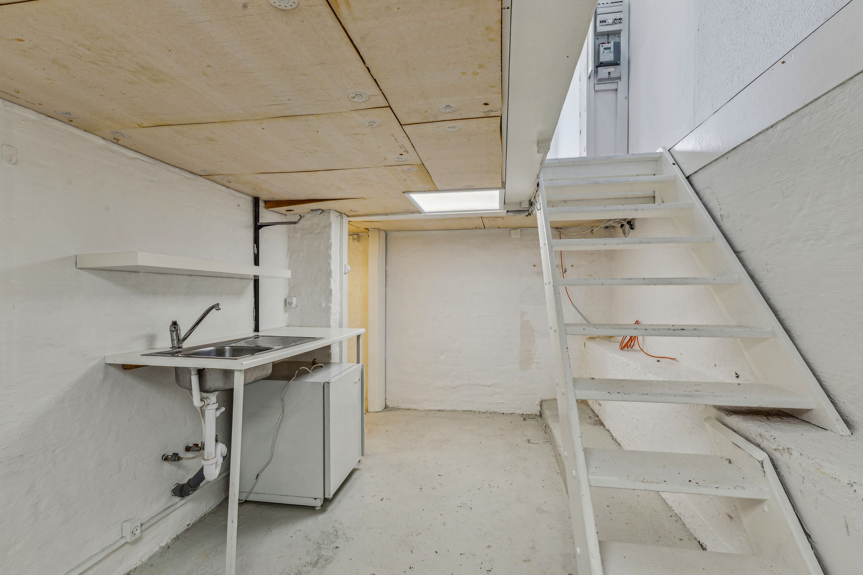 En ren, hvid vaskerum med et vask, skraldkurv og trappe til ovenfor rummet i en hvid bygning