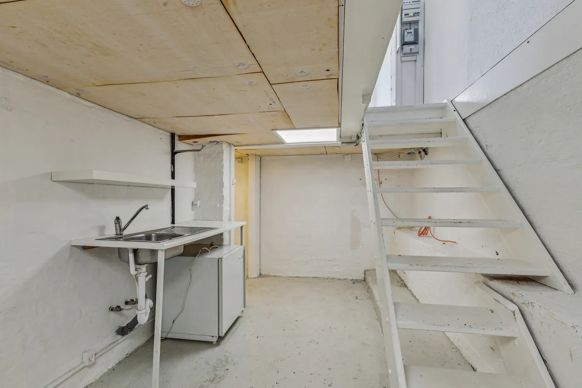 En ren, hvid vaskerum med et vask, skraldkurv og trappe til ovenfor rummet i en hvid bygning