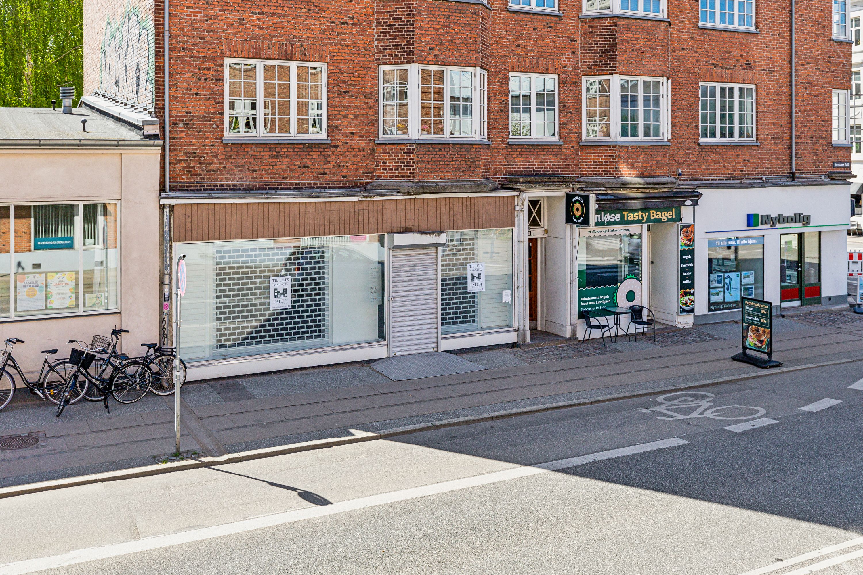 To cykler står parkeret på fortauet udenfor en lukket butik, der hedder "Holse Tasty Bagel"