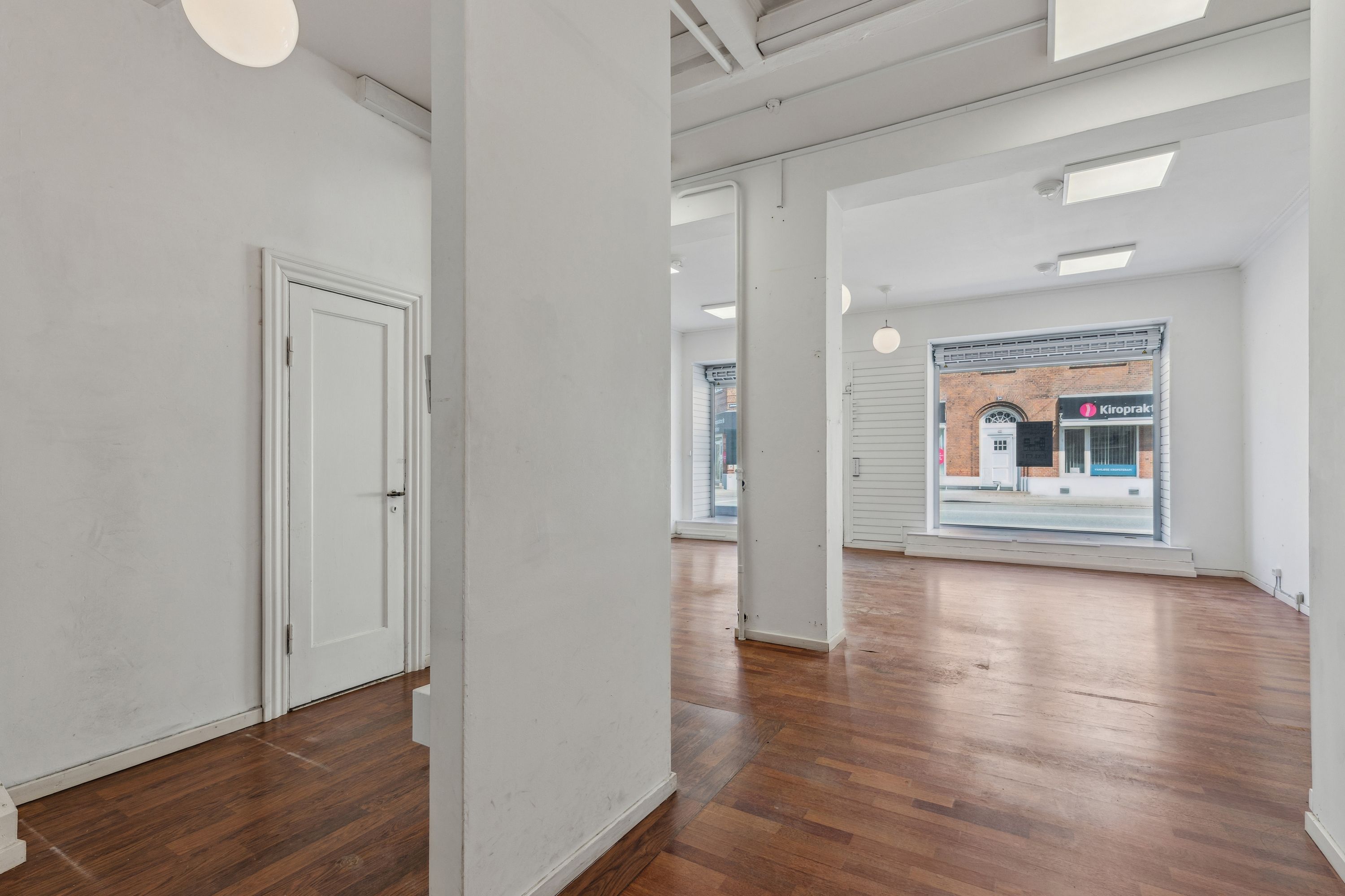 En stor og lys lejlighed med hvide vægge og trægulv, der vender ud mod en stor vinduesfront og en åben dør