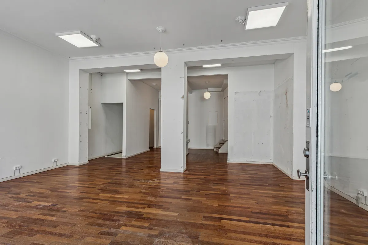 En stor stue med hårdt trægulv og hvide vægge. Der er åbne døre til siderum og lyskroner hængende fra loftet.