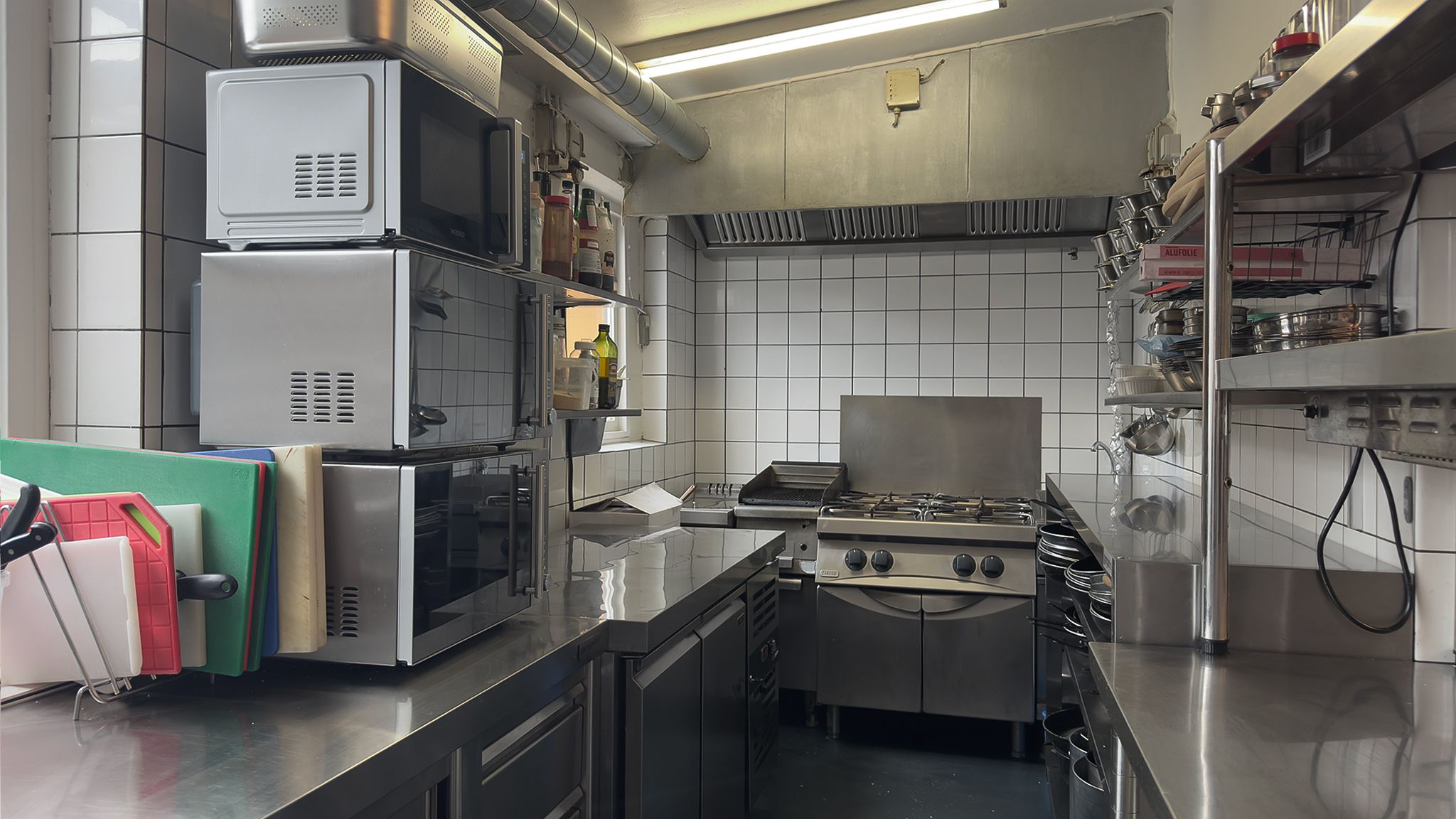 Moderne køkken med flere mikrobølgeovne, gaskomfur og flere reoler med køkkenredskaber og krydderier på høj hylde