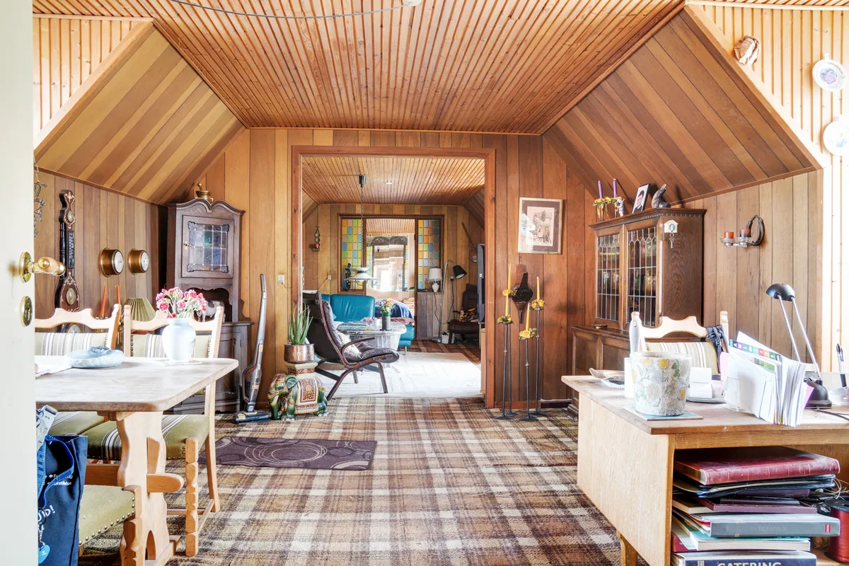 Inde i stuen med vintagemøbler og pletmønstret gulv, lysekroner, hylder og blomster. Væggene er træpaneleret, og der er