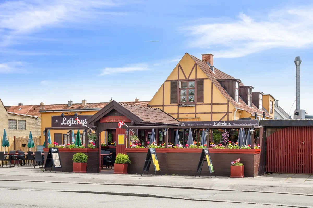 En restaurant med blomster og træstole udenfor, en rødmalet dør og et rødt tag