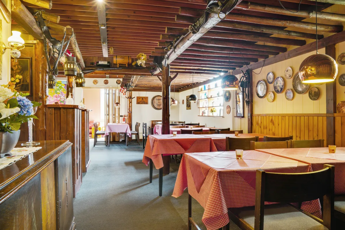 Lyst restaurant med træborde, stole og røde duge, hvor der er lysekroner, billeder og puder i stuen