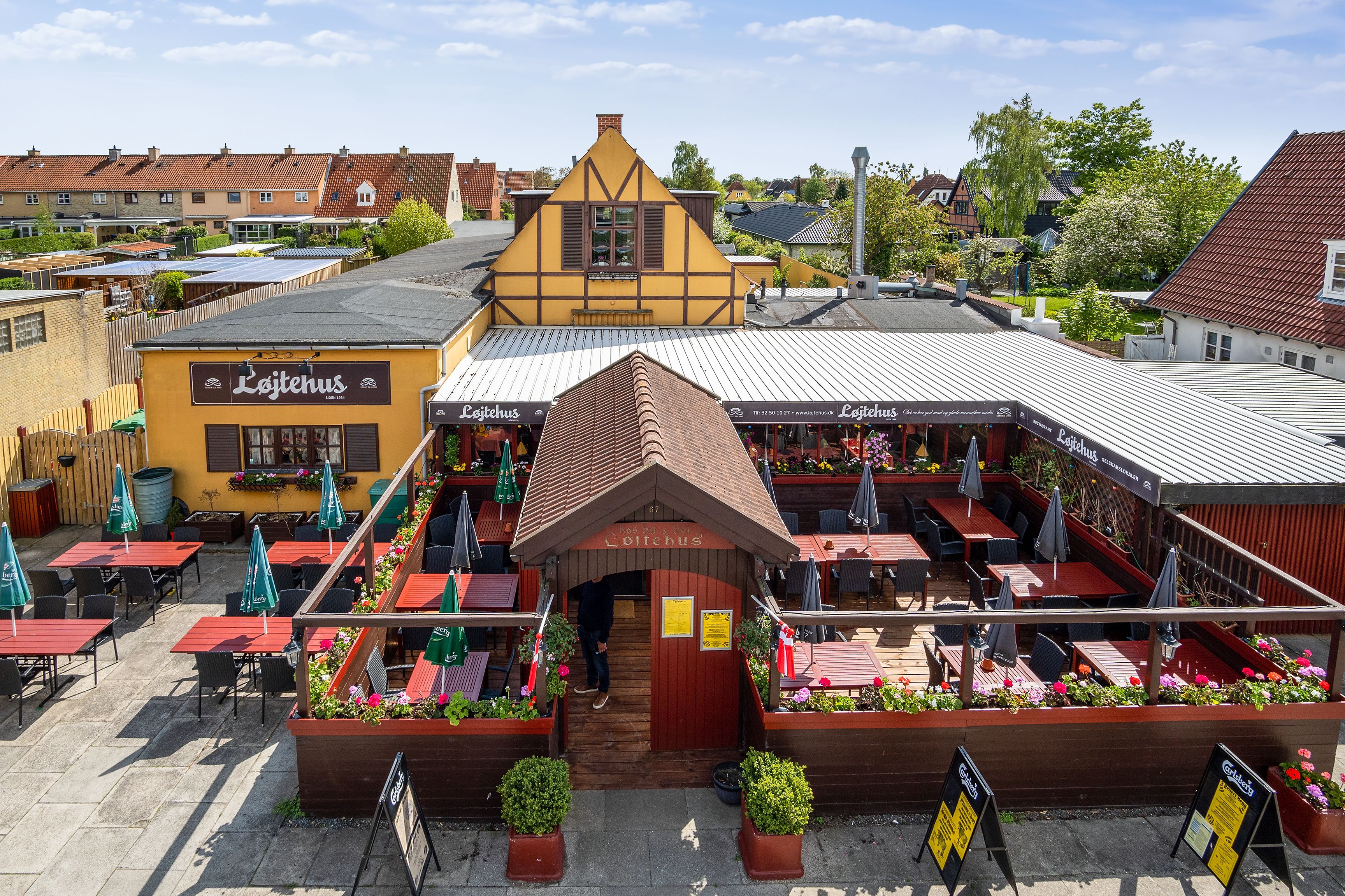Løjtehus udenfor med grønne parasoller, blomsterpotter og bord og stole med røde borde og gulv