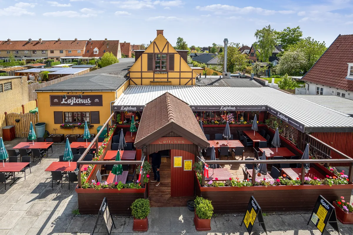 Løjtehus udenfor med grønne parasoller, blomsterpotter og bord og stole med røde borde og gulv