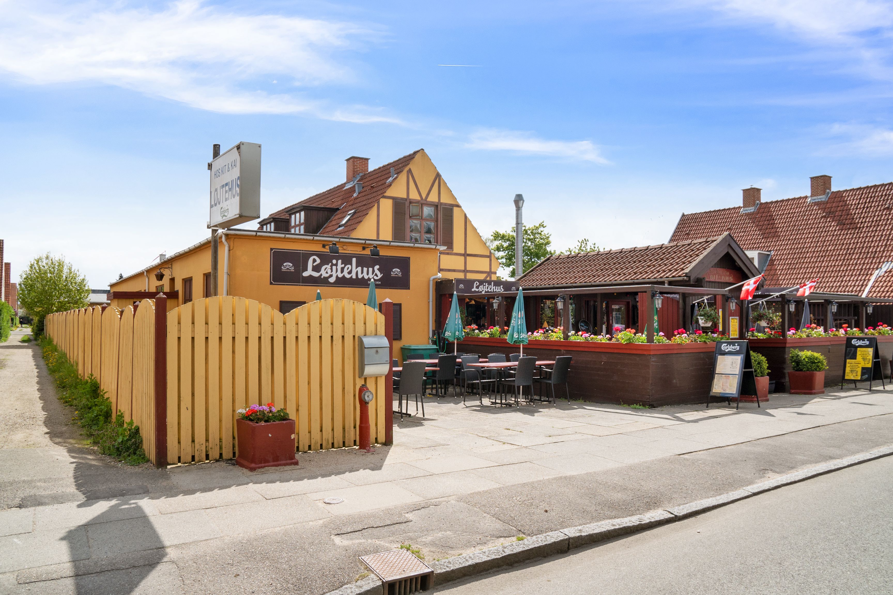 Løjtehus i Kastrup med åbent terrasseområde, hvor der er flere borde med parasoller samt en menu.