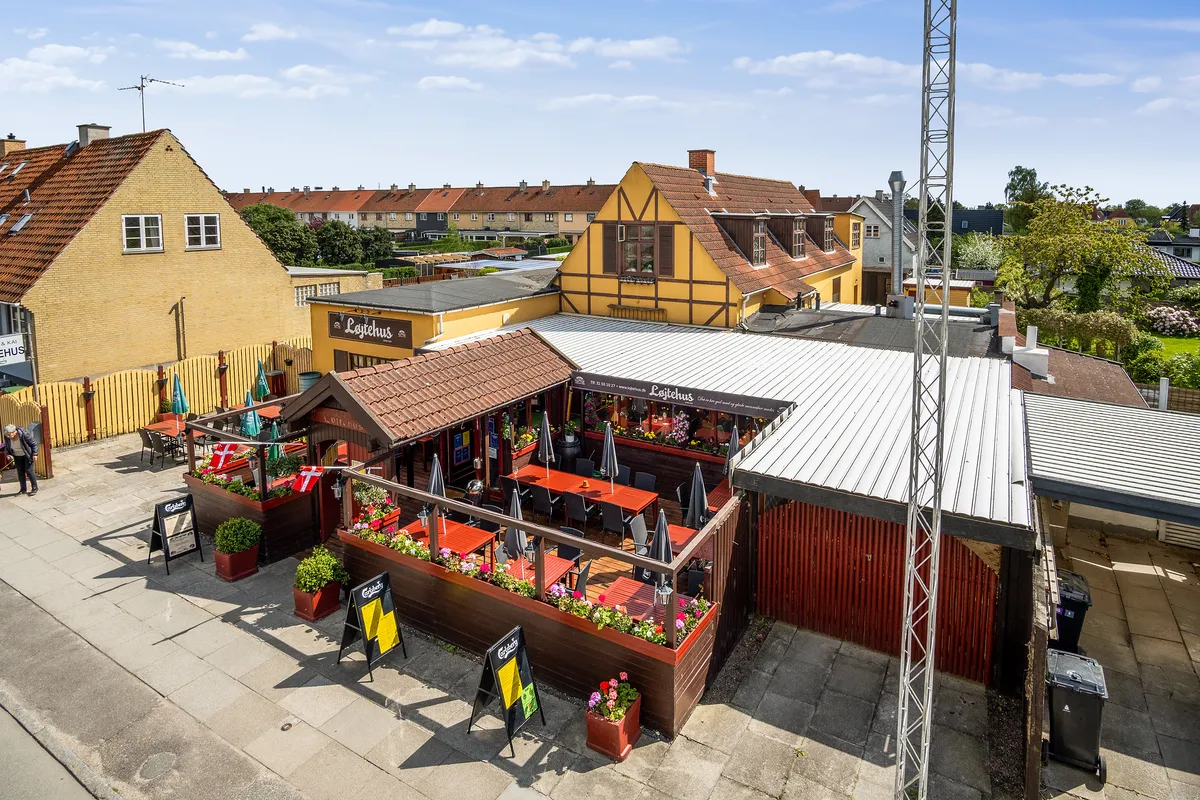 Overblik af Løjtegårds restaurant i Kastrup med terrasse og bord på forsiden. Røde og gule bygninger med blomsterpotter og
