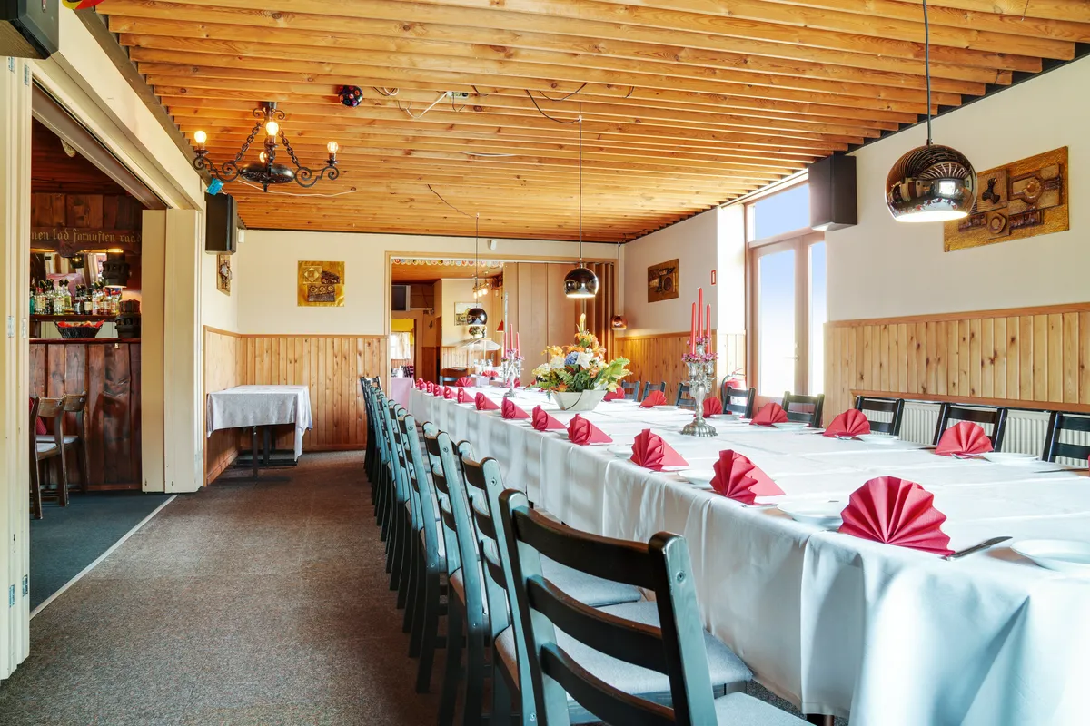 En lang række borde med hvide duge og røde servietter i en restaurant med lyse lofter og lysekroner