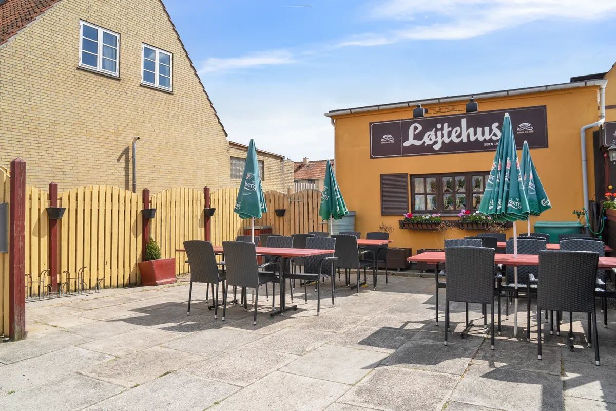 En terrasse med borde og stole og parasoller uden for Løjtehus restaurant, der er placeret i Kastrup