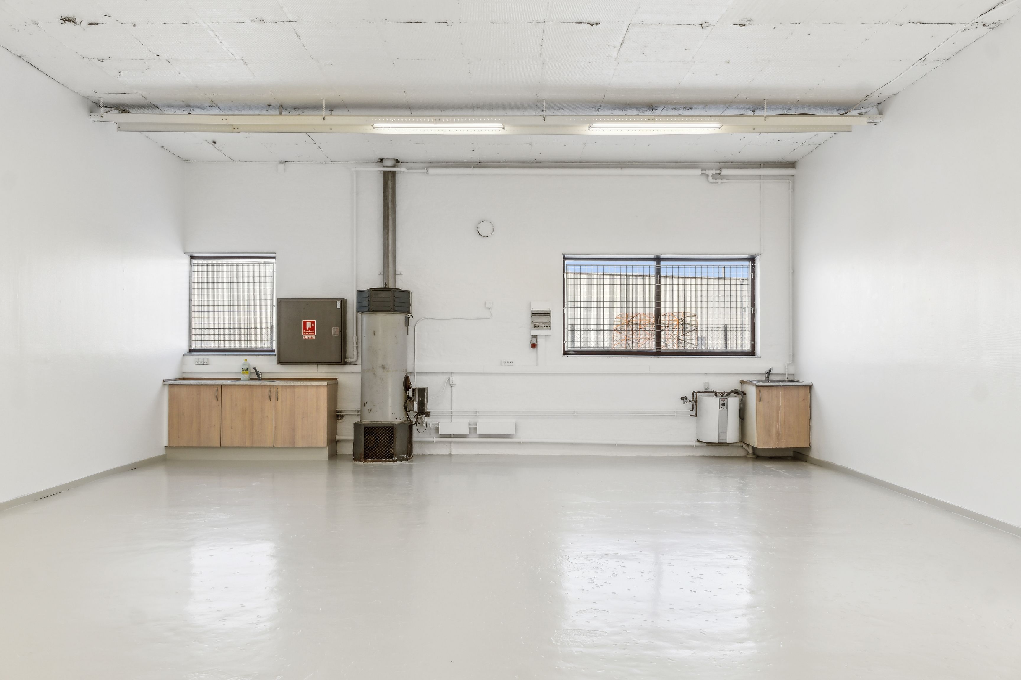 En stor, lys, tom bygningsdel med hvide vægge, loft og gulv samt to store vinduer med lyskaster