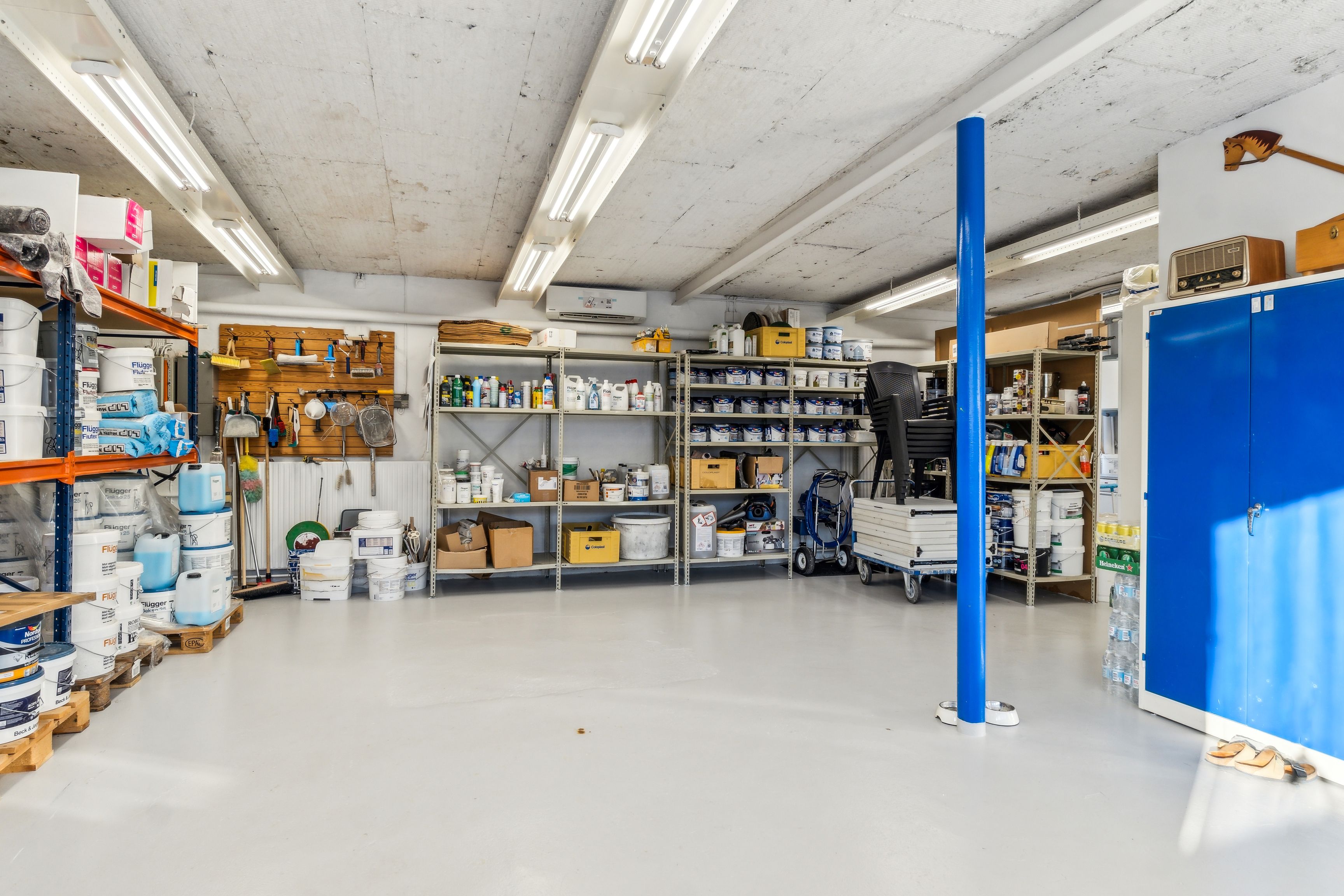 En stor lagerhal med flere hylder, kasser, plastposer, tøjstativet og tøjstativet står på gulvet og er dækket af lim.