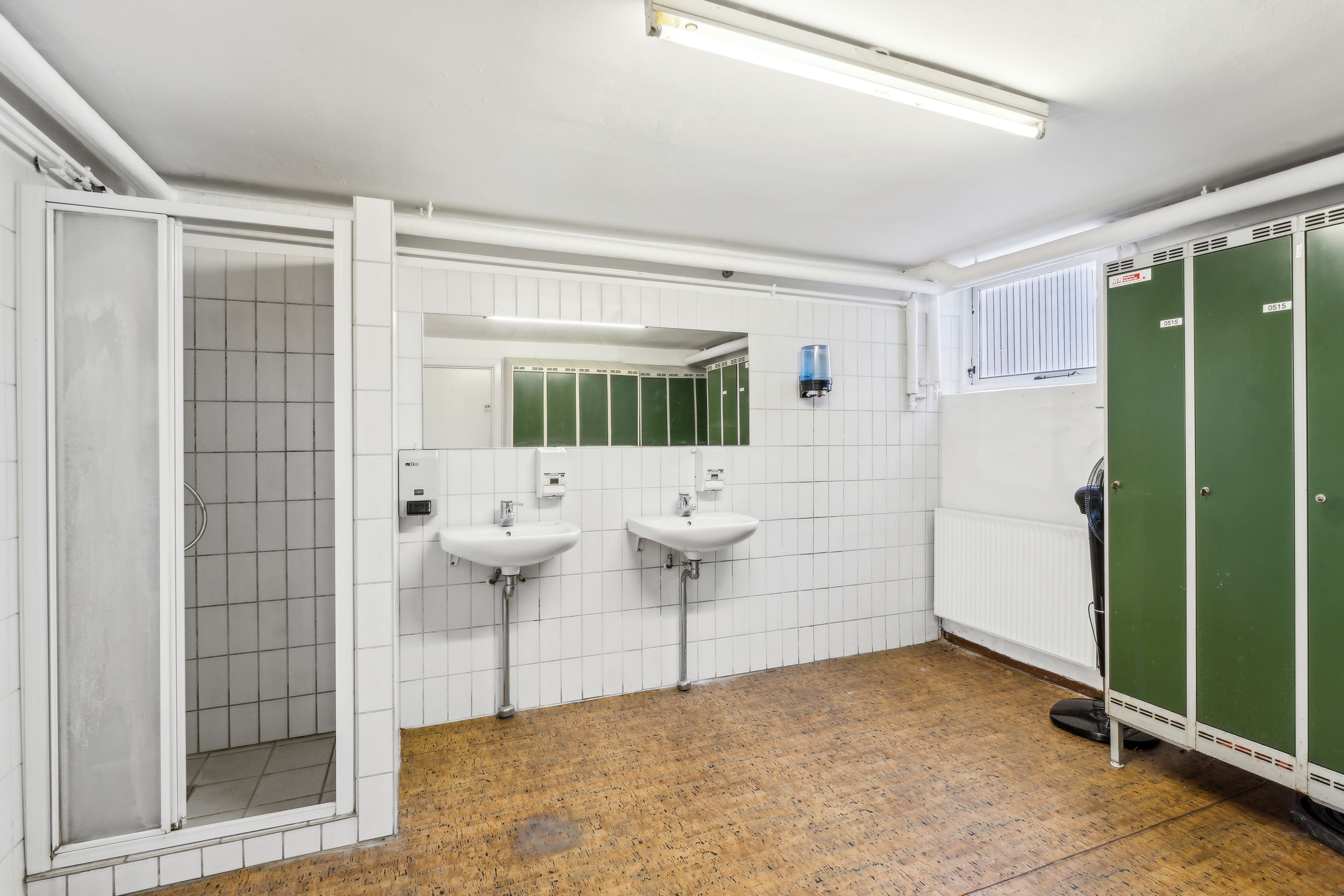 En moderne toiletrum med to hvide vasker og en radiator, hvor der er lyse, grønne, fyrretræsskabe