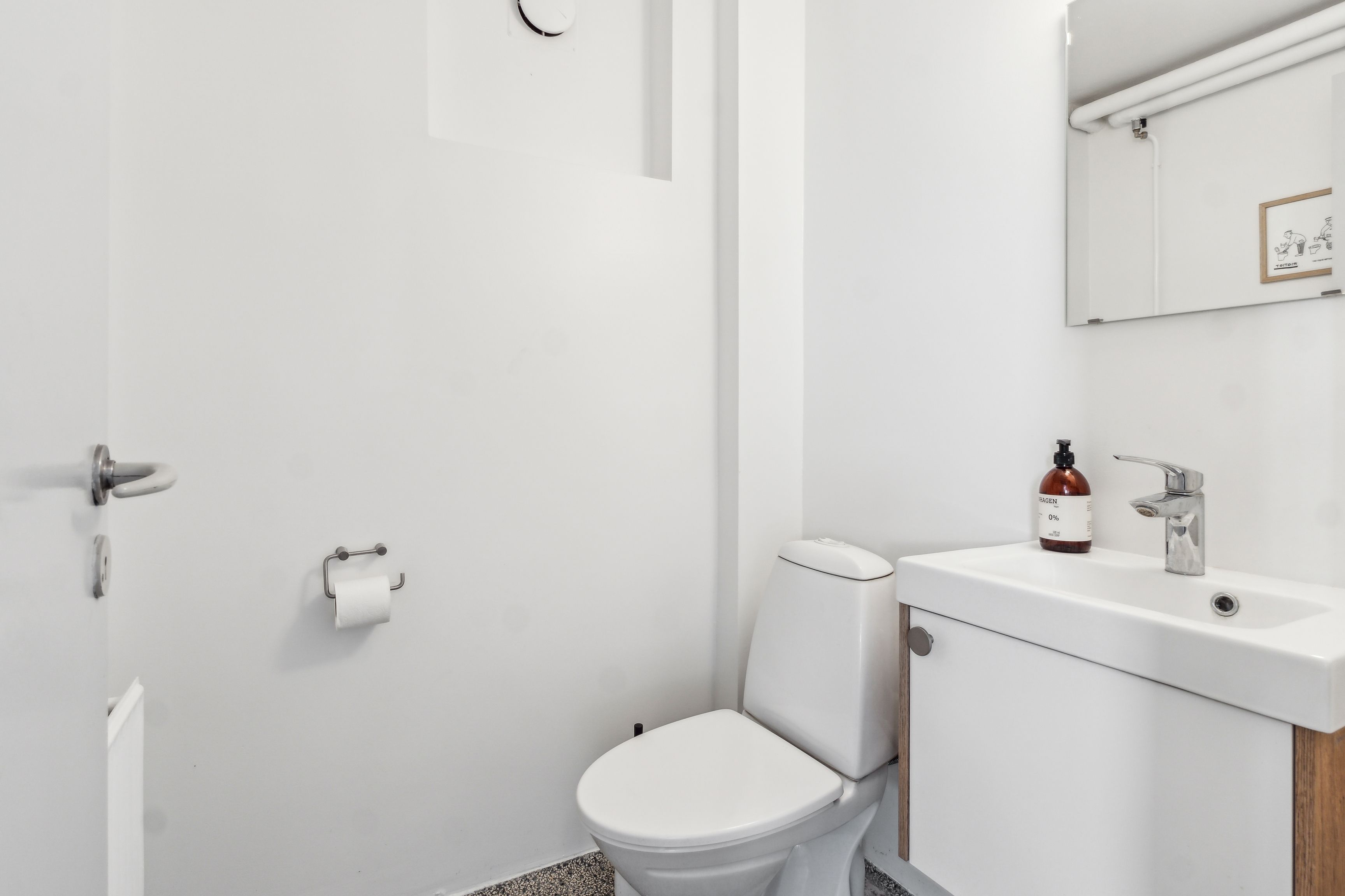 Et rent hvidt badeværelse med hvide vægge og gulv, hvor der er et toilet og en hvid vask med håndvask, og der er en