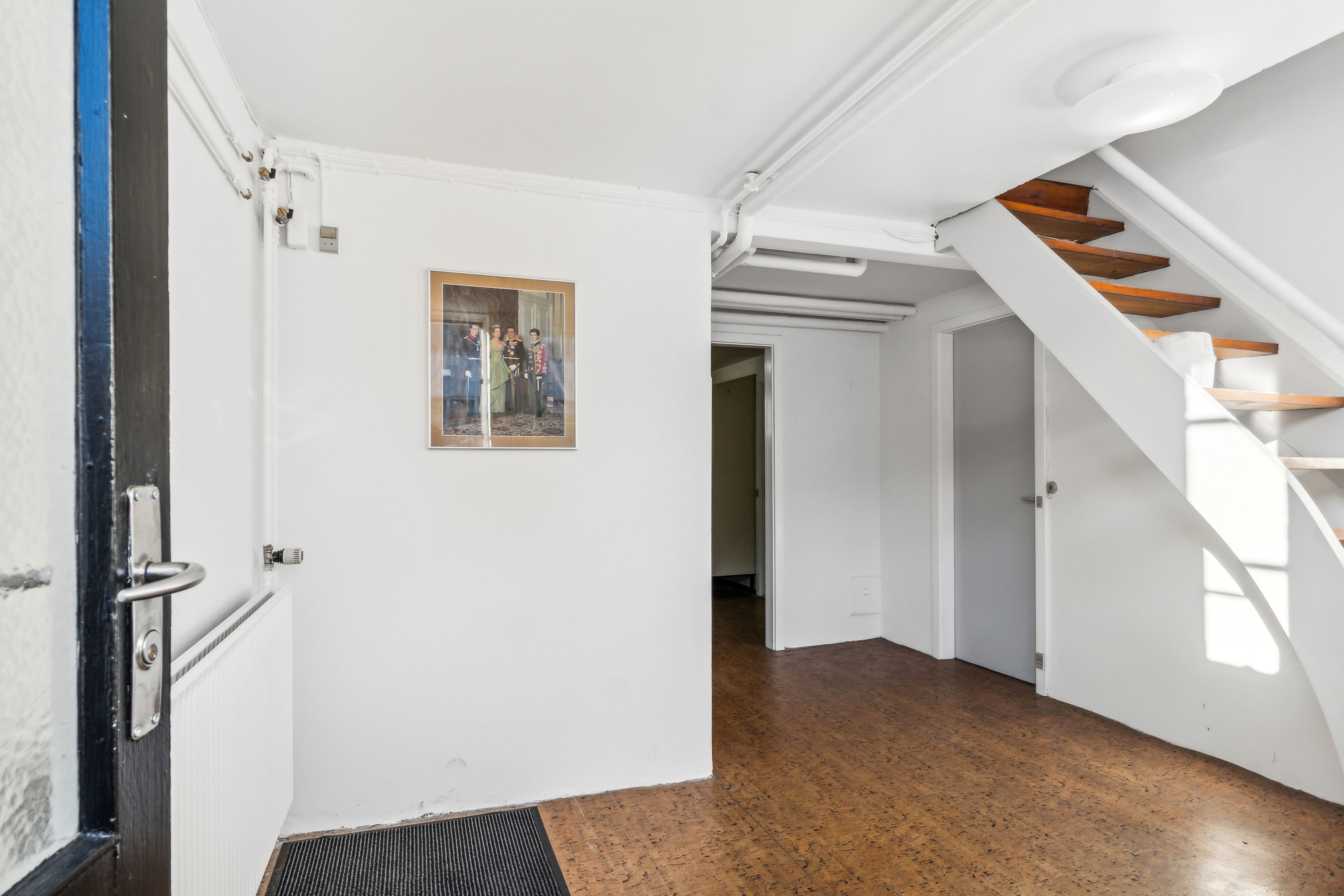 En moderne gang med lyse vægge og trægulv, et billede med en familie og et lys på loftet