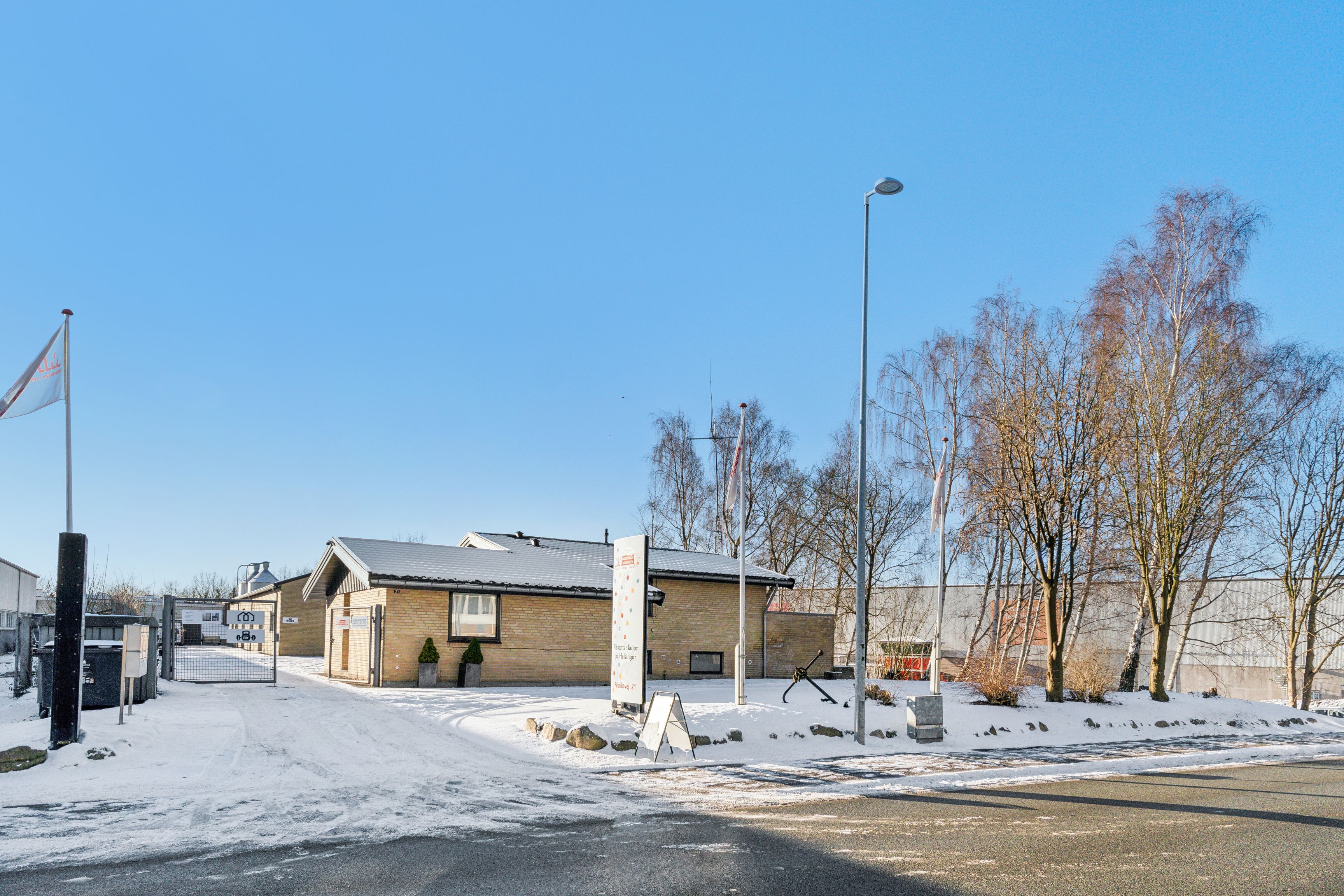 Fabriksvej 21 med sne og træer og en port til et erhvervslokale med skilt og flag
