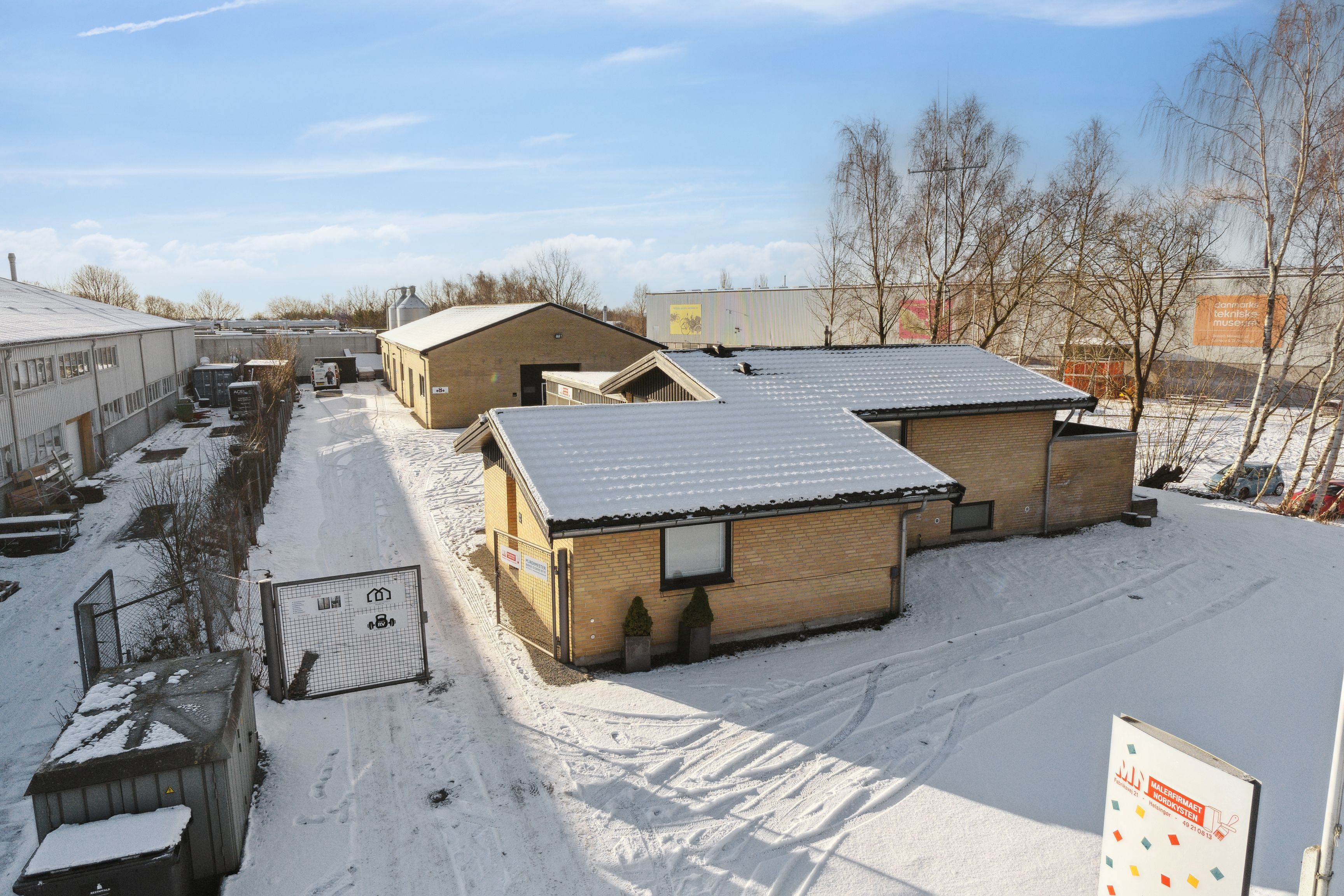 En lille gård med tre bygninger og et snedækket areal med spor fra køretøjer i en koldt dag i Helsingør