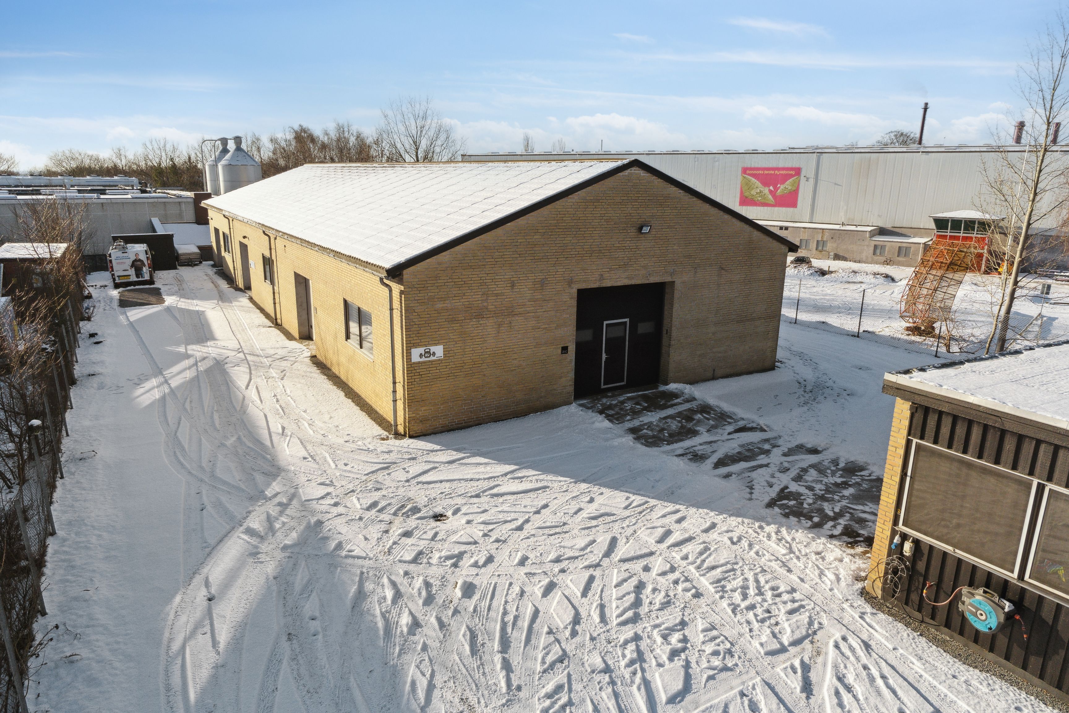 Et nybygget lagerhus i sne med tydelige kørestierspår og en hvid varevogn i baggrunden